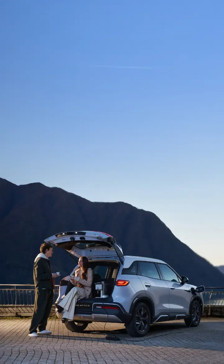 Casal a beber café, onde se vê a mulher sentada na mala do seu BYD ATTO 2